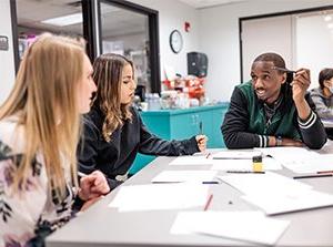 Students in a classroom discuss a group project.